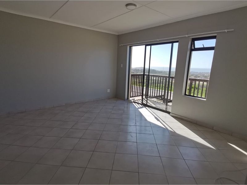 An empty, neutrally painted living area featuring tiled floors, a sliding glass door, and a window with natural light and exterior views.