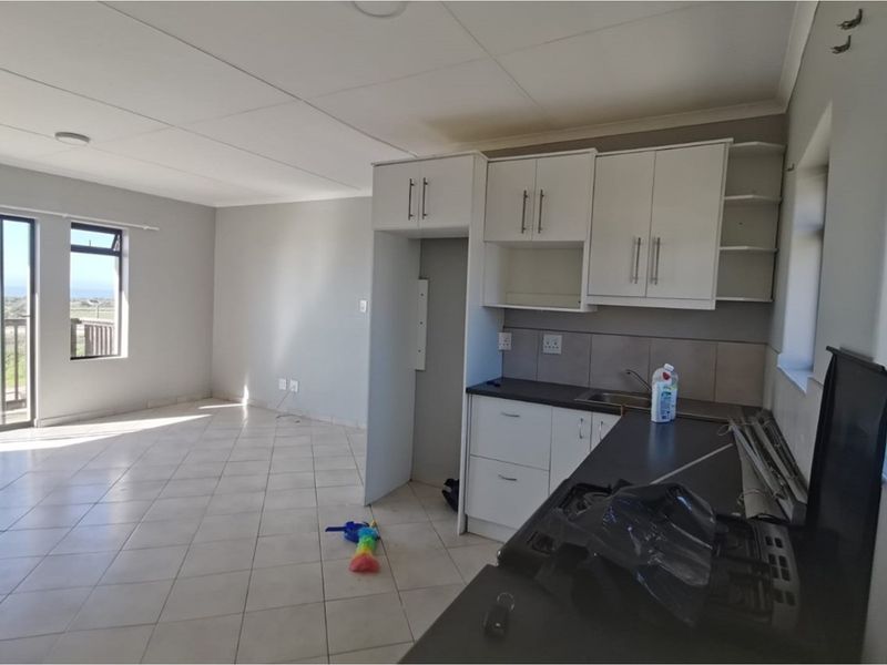 An open-plan living and kitchen area featuring tiled floors, built-in white cabinetry, and a sliding door leading to an outdoor space.