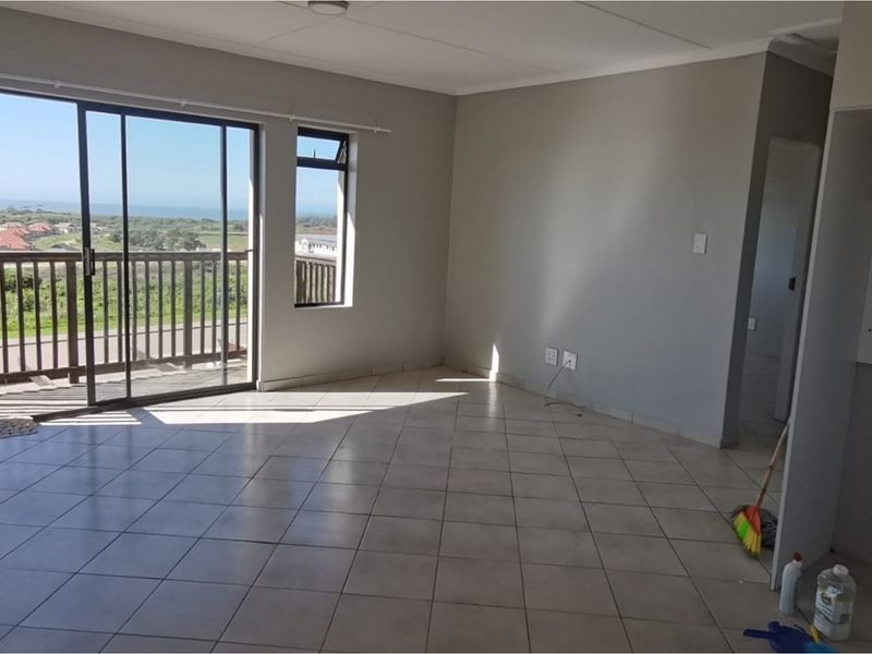 Spacious, empty living area featuring neutral tiled flooring and a large sliding glass door providing access to a balcony with scenic views.