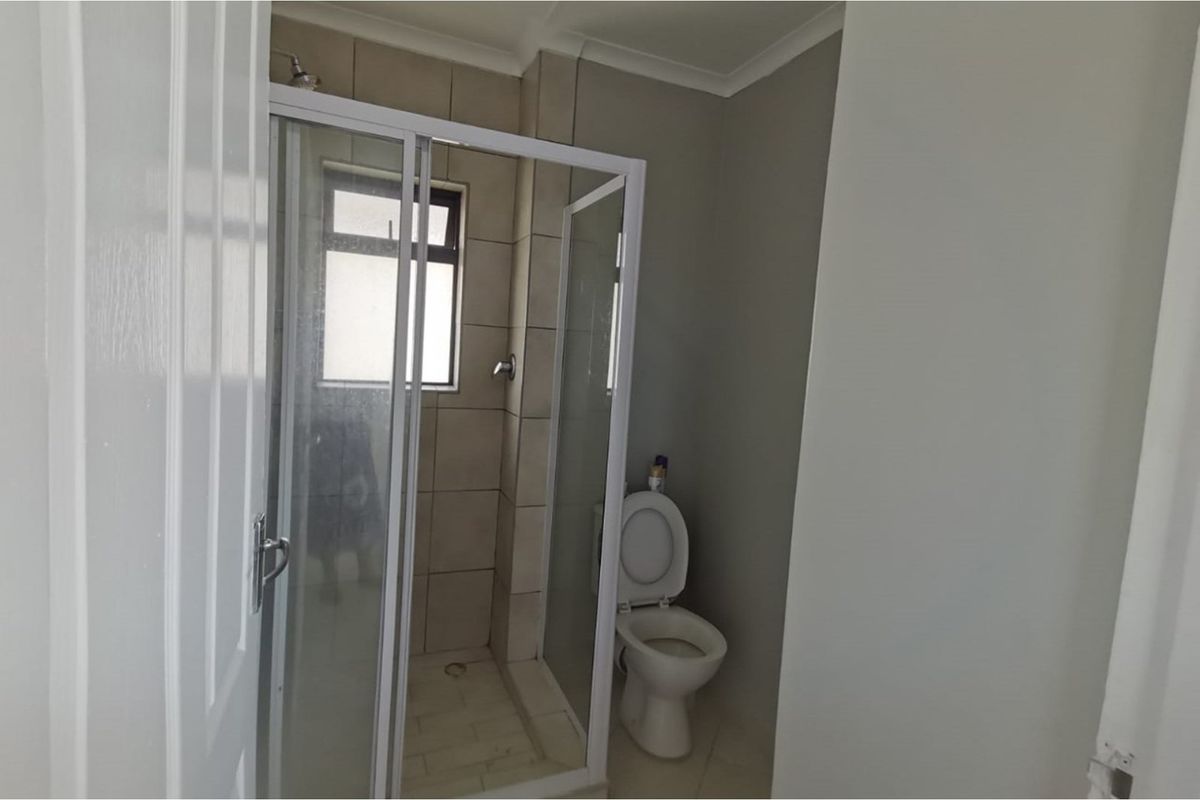 A functional bathroom featuring a glass-enclosed shower with tiled walls and a standard toilet, offering a clean and simple layout.