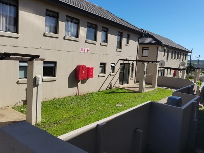 Rear exterior view of the apartment complex featuring a shared lawn area, paved patios with pergolas, and installed fire safety equipment.