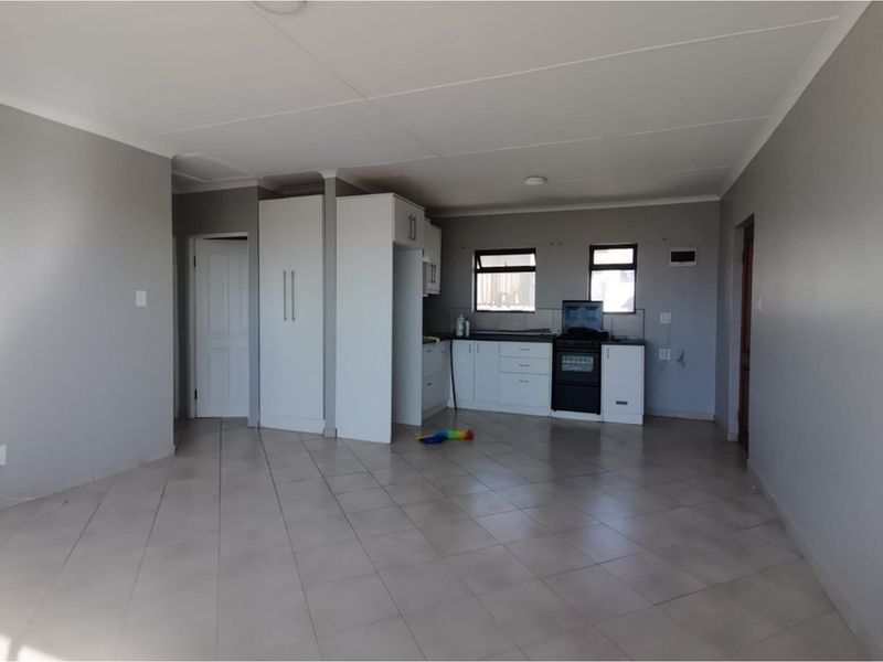 An open-plan living and kitchen area featuring neutral tiled flooring, white cabinetry, and a freestanding stove in a clean, vacant space.