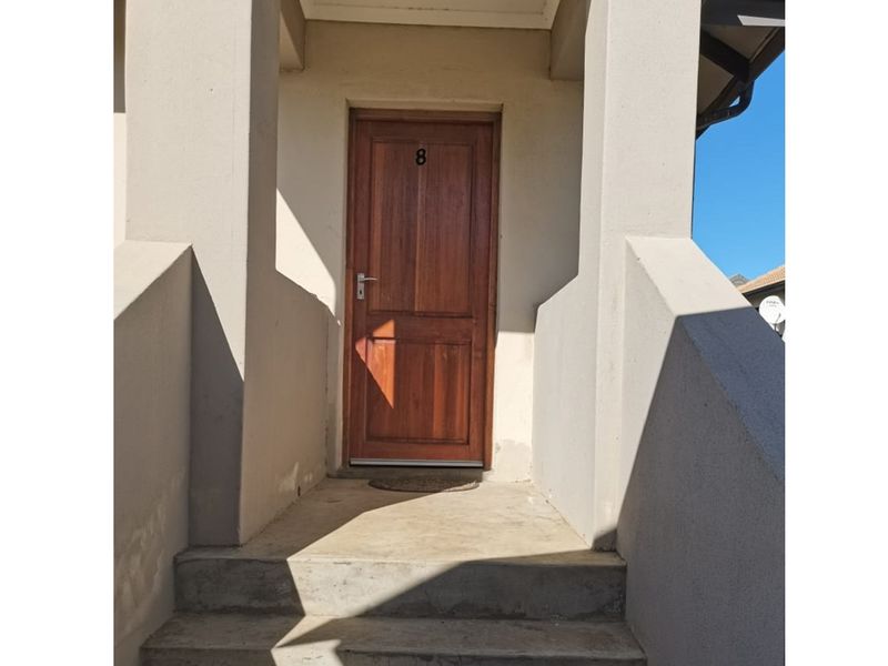 A private apartment entrance featuring a solid wooden door accessed by concrete stairs and framed by structural pillars.