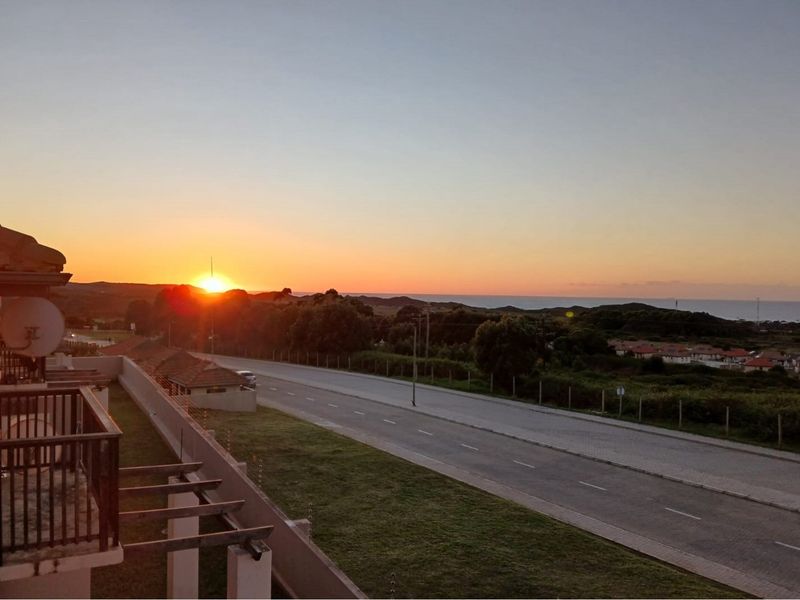 A scenic sunset view overlooking the surrounding landscape, coastal area, and local road infrastructure from an elevated balcony position.