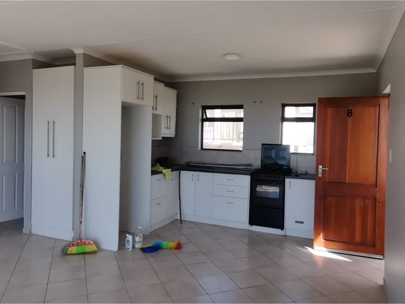 Open plan kitchen area featuring white cabinetry, tiled flooring, and a solid timber entrance door in a neutral living space.