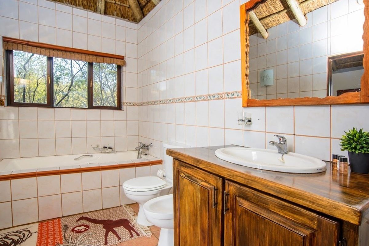 A rustic bathroom featuring a built-in bathtub, vanity with basin, toilet, bidet, and exposed thatch roof detailing.