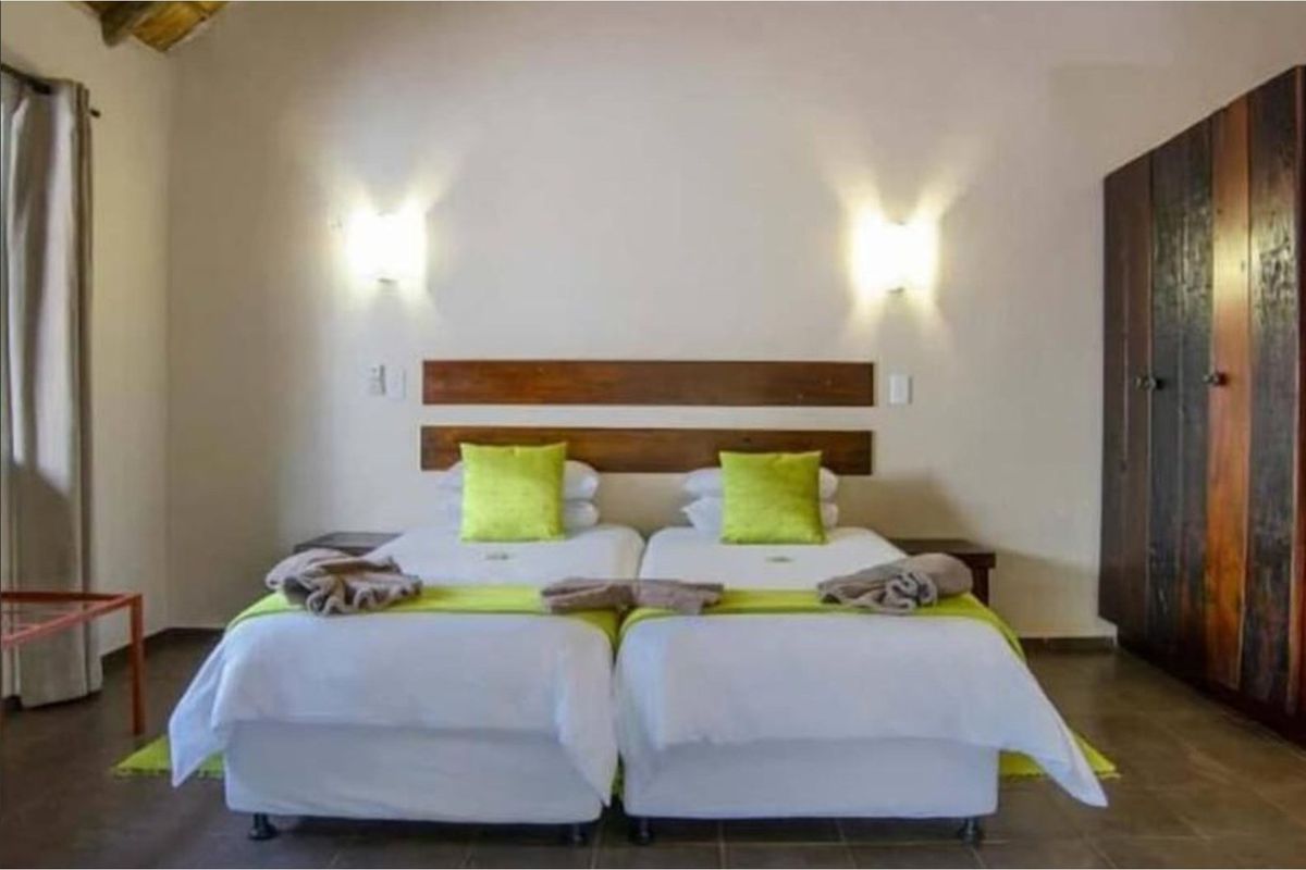 A well-maintained bedroom featuring a built-in wooden headboard, wall-mounted lighting, and a large dark wood wardrobe.