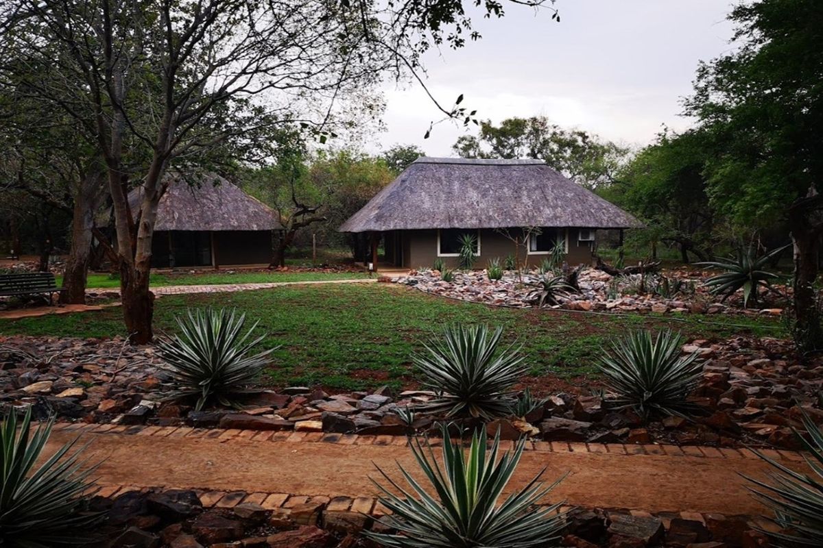 A view of the farm property featuring traditional thatched-roof structures set within a landscaped garden with rockery and established trees.