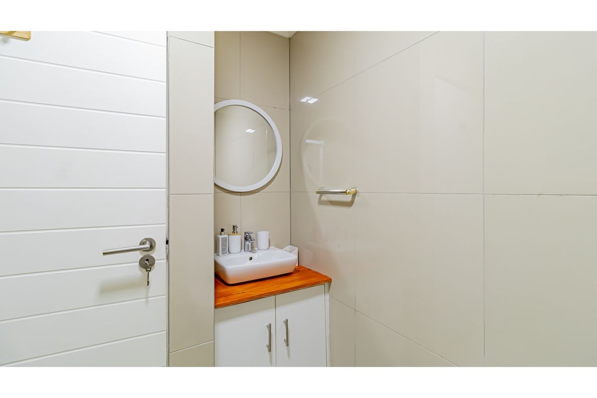 A modern bathroom featuring a vanity with a wooden countertop, a vessel sink, a circular mirror, and neutral wall tiling.