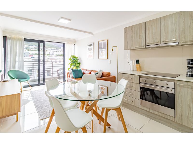 Modern open-plan living area featuring a sleek kitchen with built-in oven and hob, flowing seamlessly to a balcony with urban views.