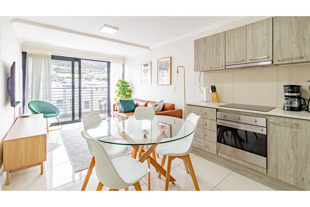Modern open-plan living area featuring a sleek kitchen with built-in oven and hob, flowing seamlessly to a balcony with urban views.