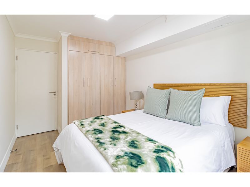 A well-maintained bedroom featuring built-in light wood cabinetry, light timber-look flooring, and a modern neutral aesthetic.