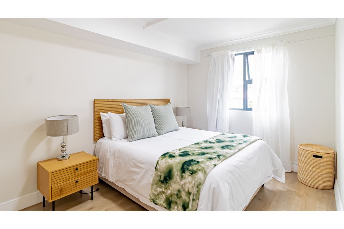 A bright and well-maintained bedroom featuring light wood-look flooring, neutral walls, and a window with natural light.
