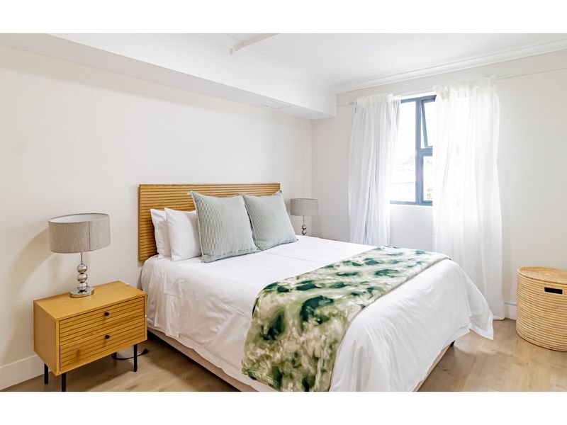 A bright and well-maintained bedroom featuring light wood-look flooring, neutral walls, and a window with natural light.