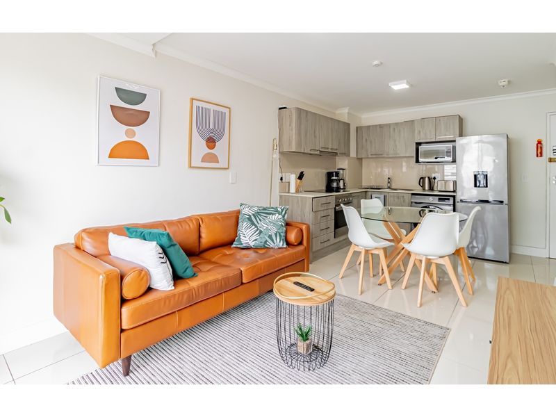 An open-plan living and kitchen area featuring modern cabinetry, integrated appliances, and tiled flooring in a well-maintained apartment setting.