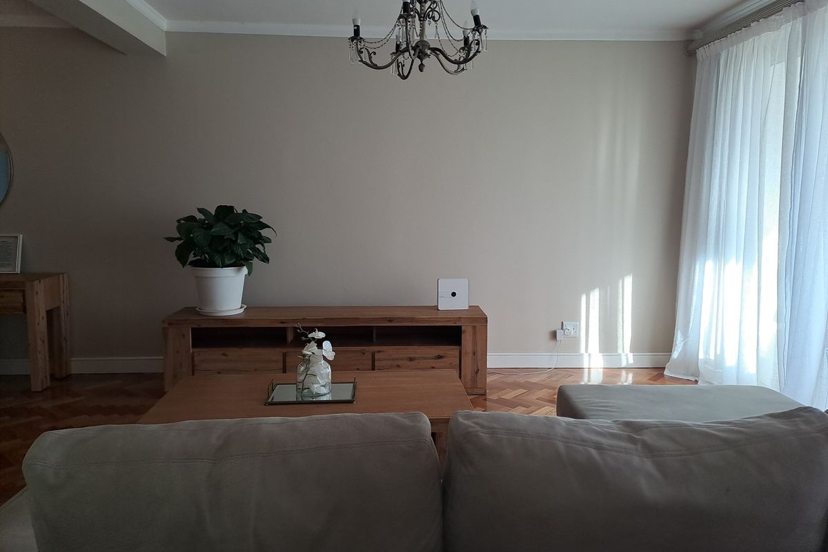 A well-maintained living room featuring classic parquet flooring, neutral wall tones, and an elegant chandelier, offering a bright and inviting atmosphere.