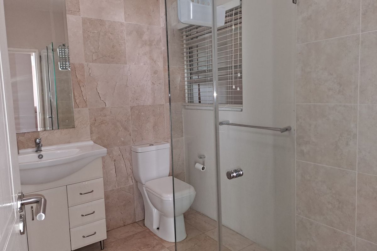 A modern bathroom featuring a glass-enclosed shower, a vanity with integrated basin, and neutral stone-look wall tiling.