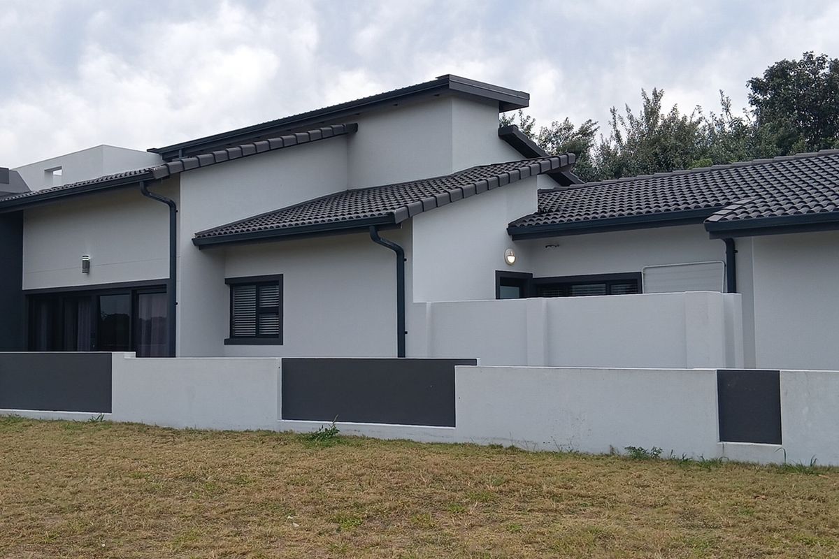A modern rear elevation of the house featuring a tiled roof, clean rendered walls, and a contemporary boundary wall with integrated lighting.