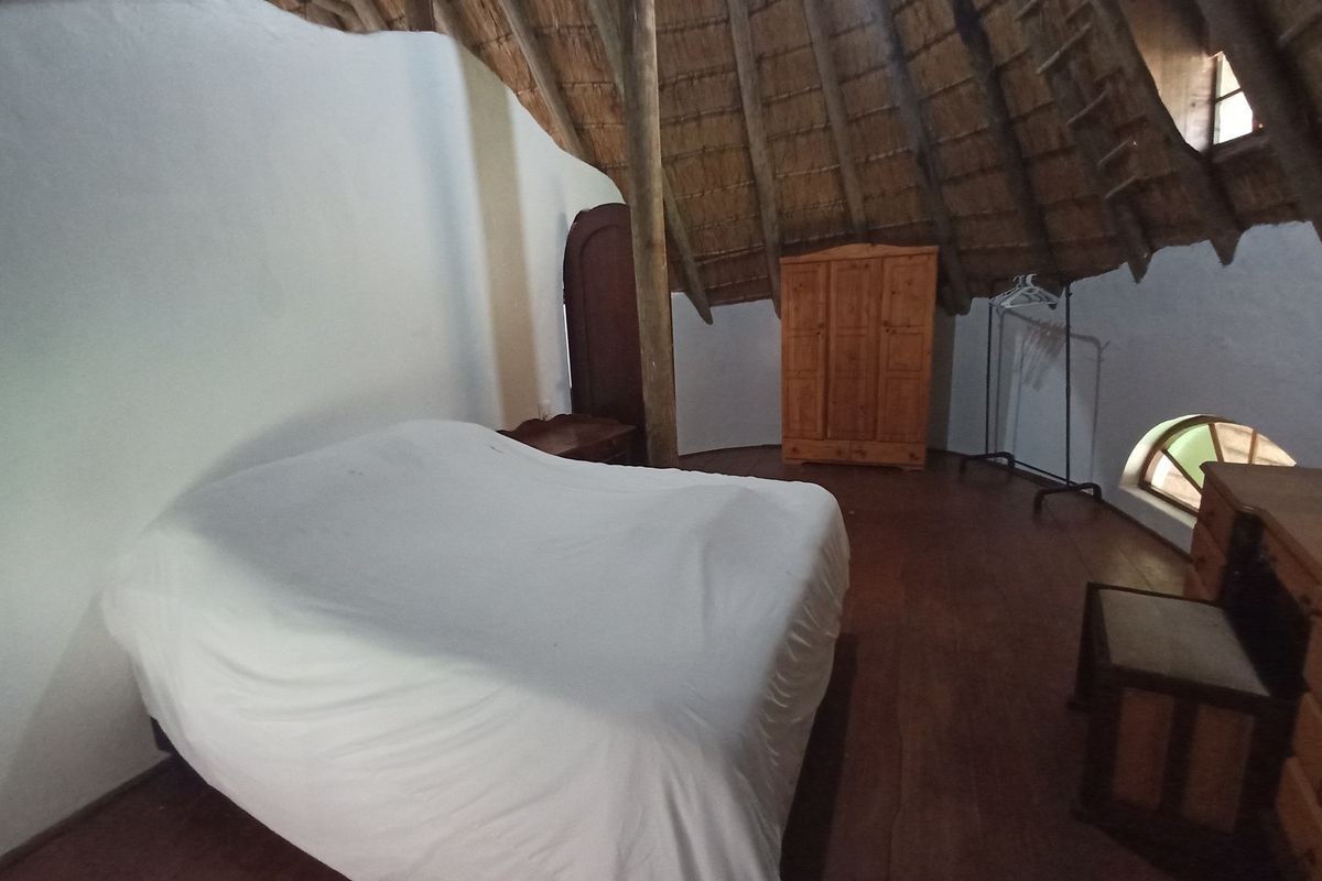 A rustic bedroom featuring a traditional thatched roof, exposed timber structural elements, and arched windows, offering a unique architectural character.