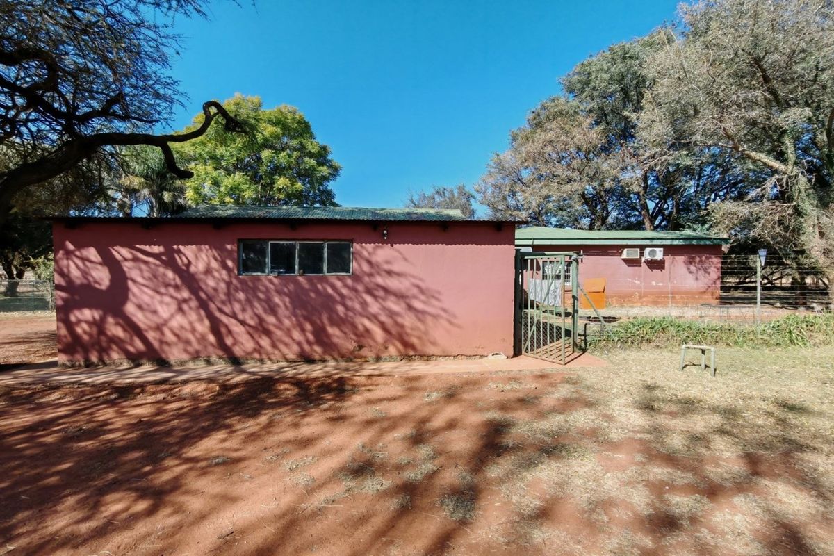 Exterior view of a farm building featuring a red painted facade, metal roofing, and a metal security gate set within a rural landscape.