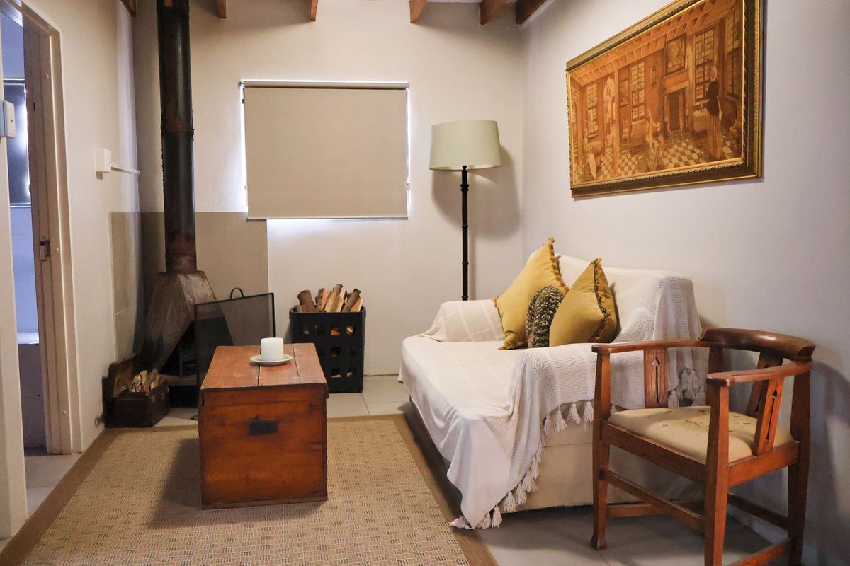 A cozy living room featuring a built-in wood-burning fireplace with an exposed flue and exposed timber ceiling beams.