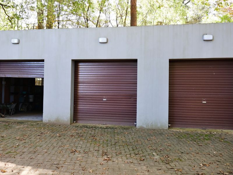 A triple garage featuring brown roller shutter doors and exterior wall-mounted lighting, set against a paved driveway area.