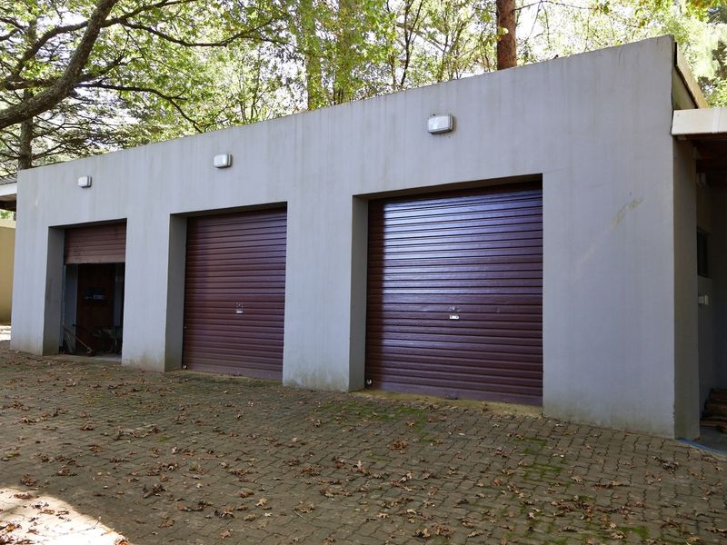 A triple garage structure featuring brown roller shutter doors and exterior wall-mounted lighting, set against a paved driveway area.