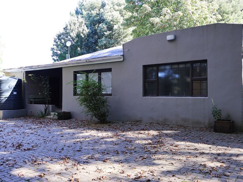 Exterior view of the property featuring a paved driveway, water storage tank, and dark-framed windows set against a neutral rendered facade.