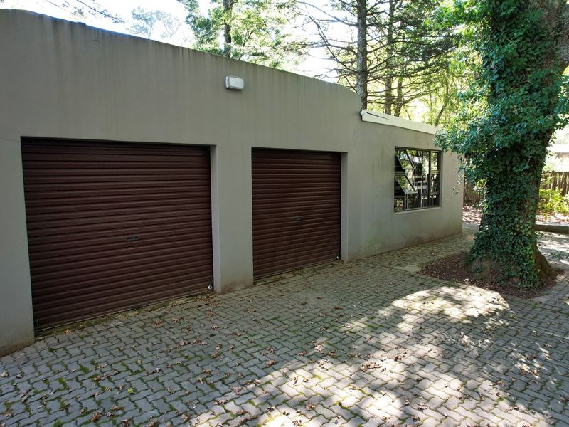 A double garage with roller shutter doors and paved driveway, situated in a wooded setting.