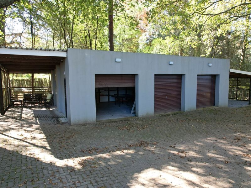 A triple garage structure featuring roller shutter doors and an adjacent covered patio area, set within a wooded garden environment.