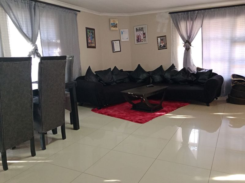 A spacious living area featuring neutral tiled flooring and large windows with curtain rails, providing a bright and functional space.