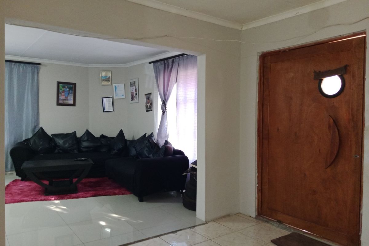 A living room area featuring tiled flooring and a wooden entrance door, with an open-plan layout connecting to the main lounge space.
