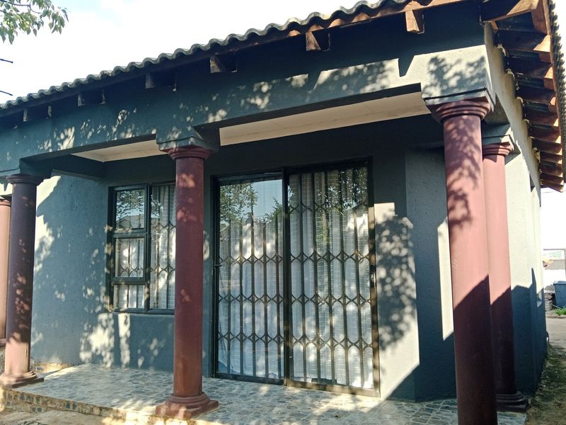 A covered patio area featuring decorative columns, tiled flooring, and a sliding glass door with a security gate.