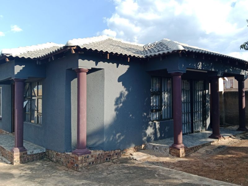 A single-story house featuring a dark grey facade, decorative columns, a tiled roof, and a covered patio area with security gates.