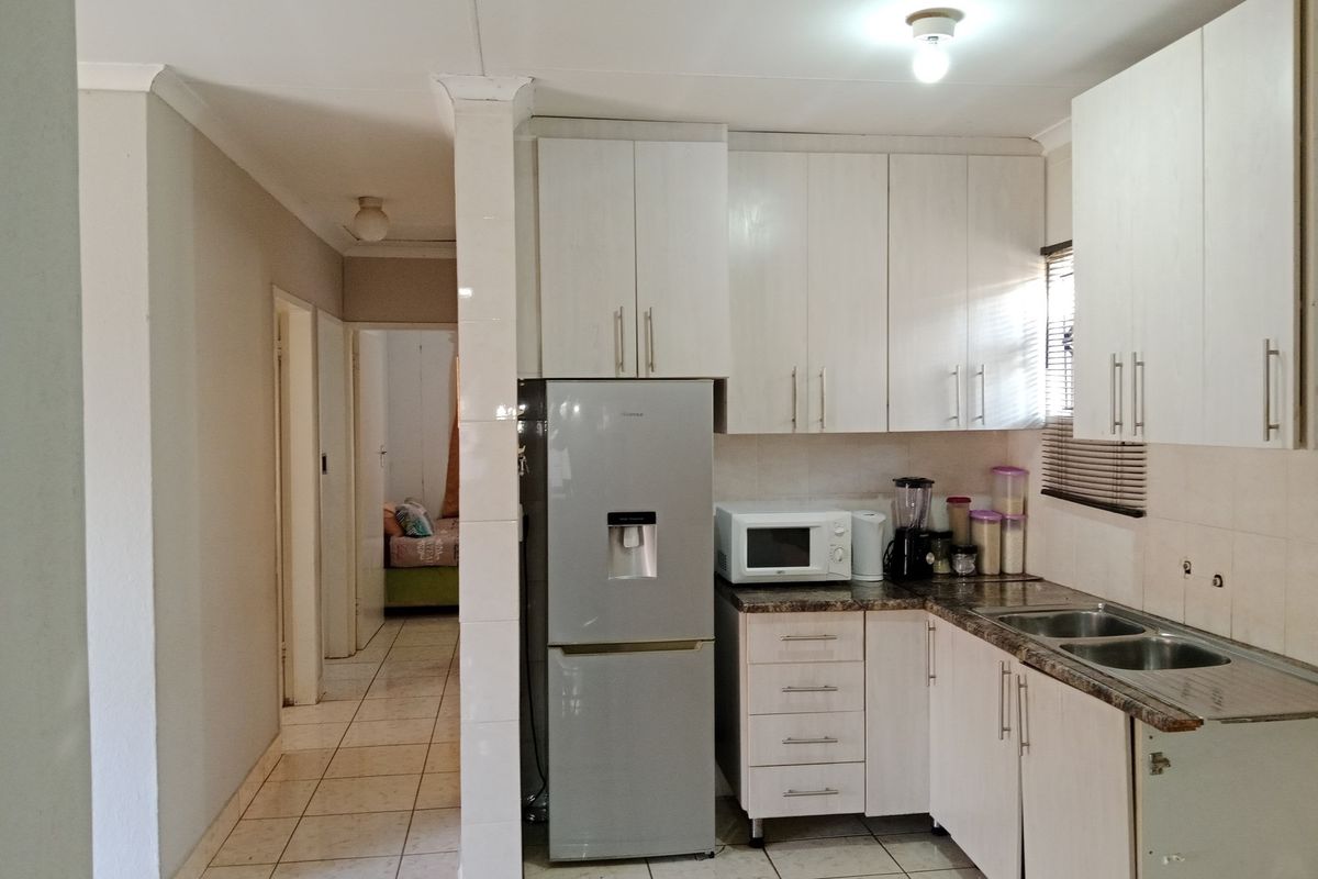 Compact kitchen featuring white built-in cabinetry, laminate countertops, and a double bowl sink, with tiled flooring extending into the adjacent hallway.