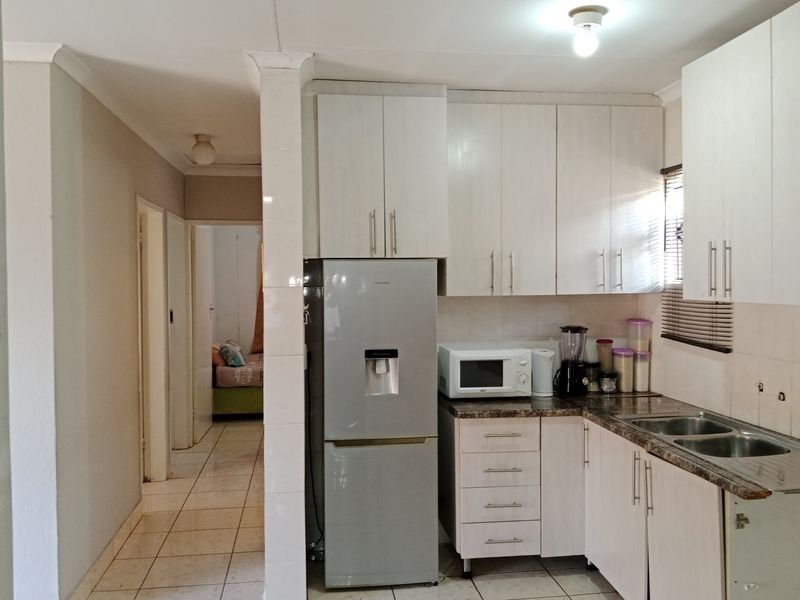 Compact kitchen featuring white built-in cabinetry, laminate countertops, and a double bowl sink, with tiled flooring extending into the adjacent hallway.