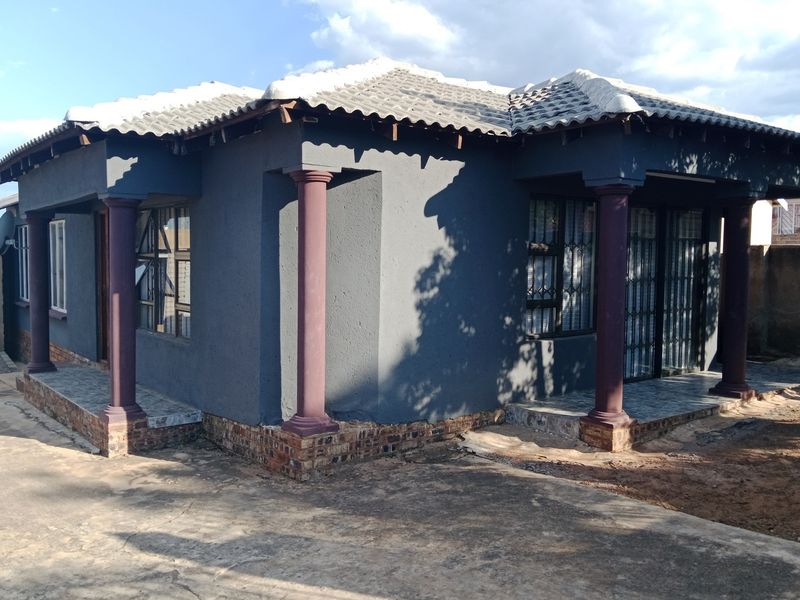 Front view of a single-story house featuring a tiled roof, decorative columns, and a paved driveway area.