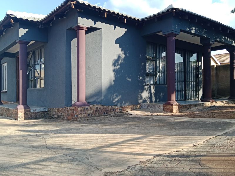 Front exterior view of a house featuring a covered patio with decorative columns, security gates, and a concrete driveway.