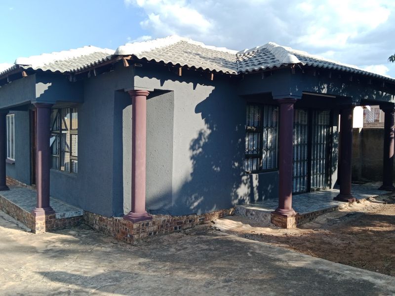 A single-story house featuring a dark grey exterior, tiled roof, and decorative columns with a tiled patio area.