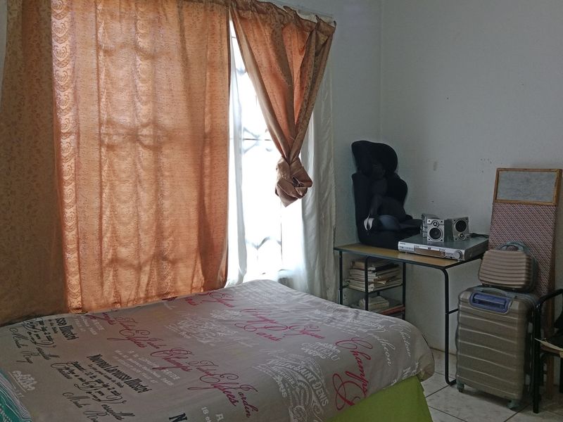 A functional bedroom featuring tiled flooring and a window fitted with security bars, providing natural light.
