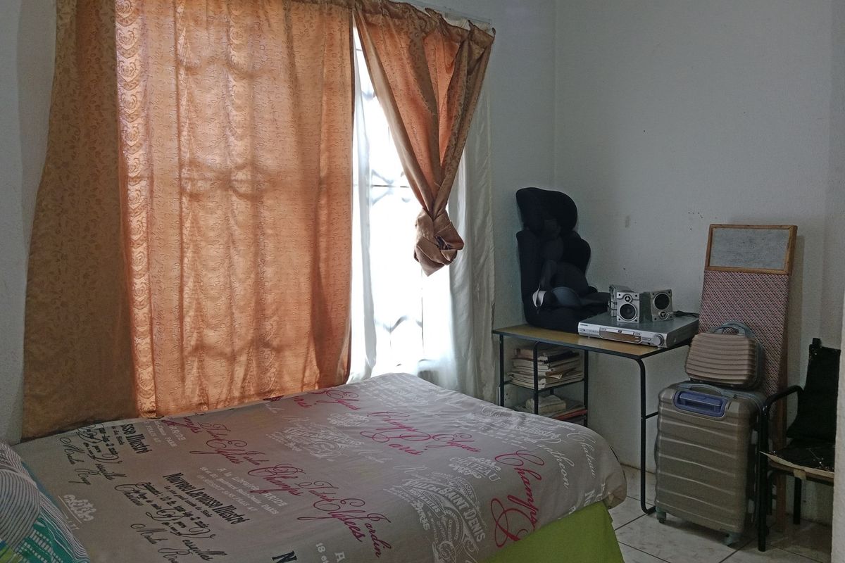 A functional bedroom featuring tiled flooring and a window fitted with security bars, providing natural light.