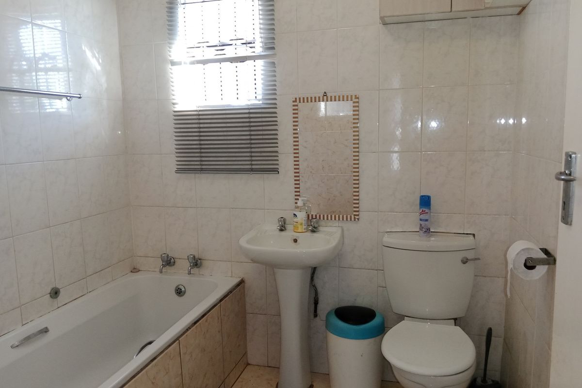 A functional bathroom featuring a pedestal basin, bathtub, and toilet with neutral wall and floor tiling.