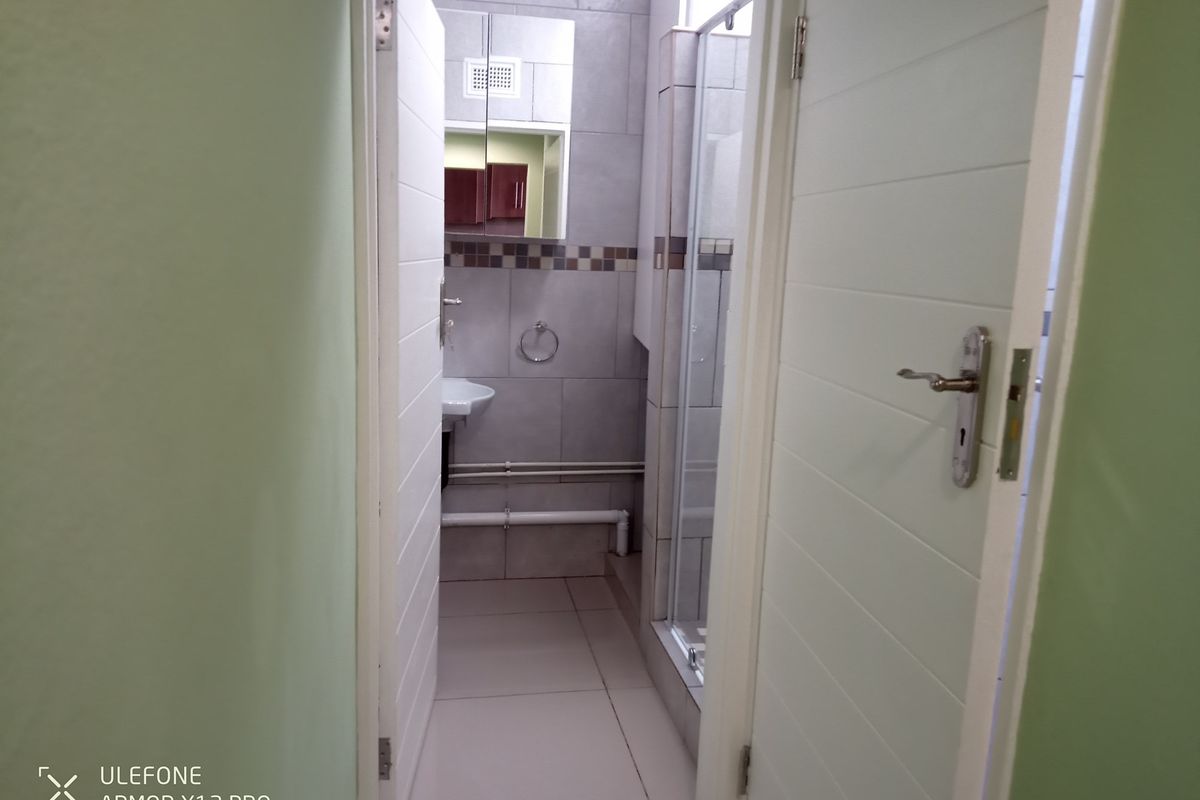 A compact bathroom featuring a shower enclosure, wall-mounted basin, and mirrored medicine cabinet with neutral floor and wall tiling.