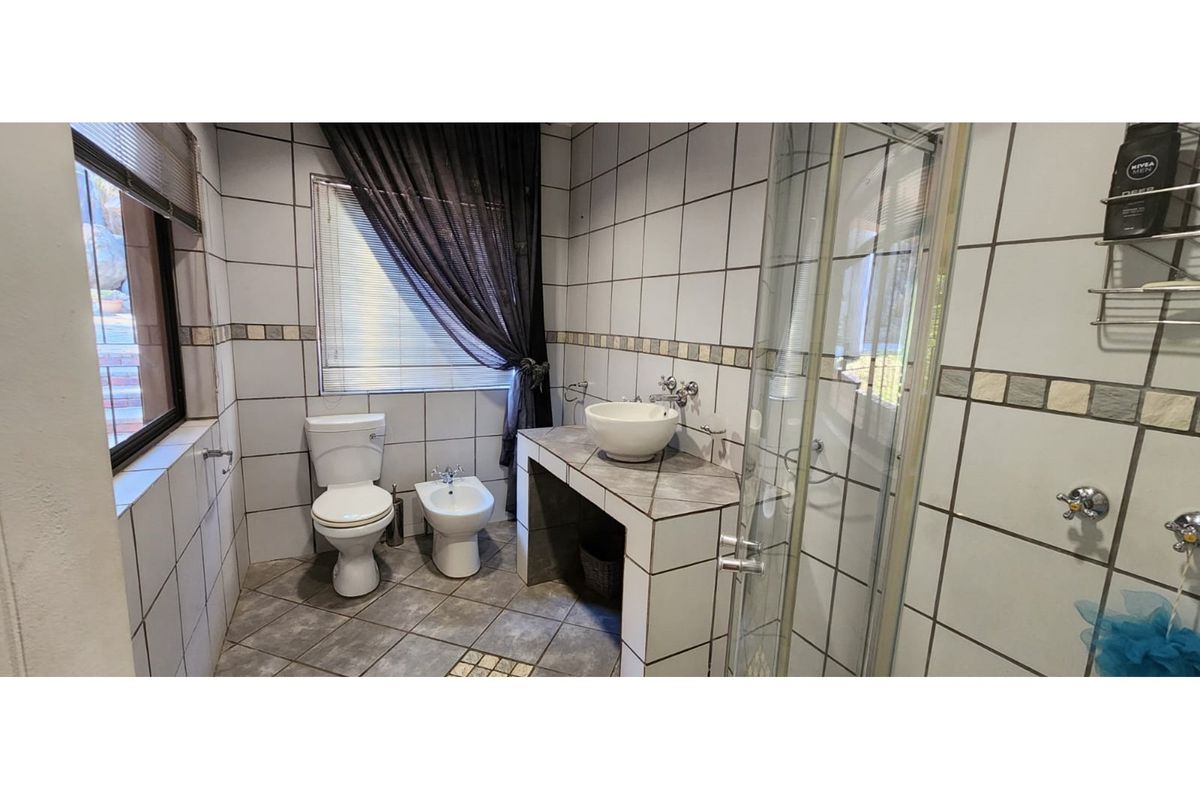 A functional bathroom featuring a tiled shower enclosure, a vessel sink vanity, a toilet, and a bidet with neutral wall tiling.