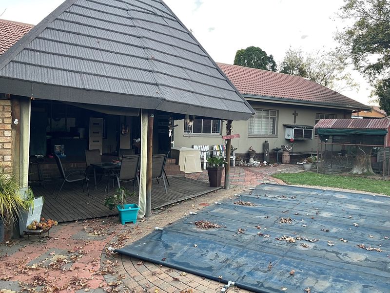 Outdoor entertainment area featuring a covered patio with timber decking, overlooking a swimming pool with a protective cover and a paved garden area.