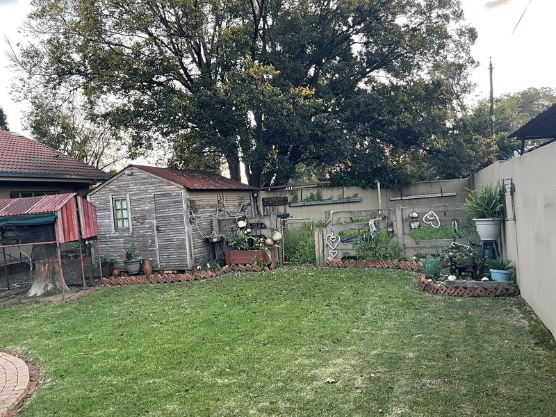 A rear garden area featuring a lawn, a weathered timber storage shed, and perimeter boundary walls.