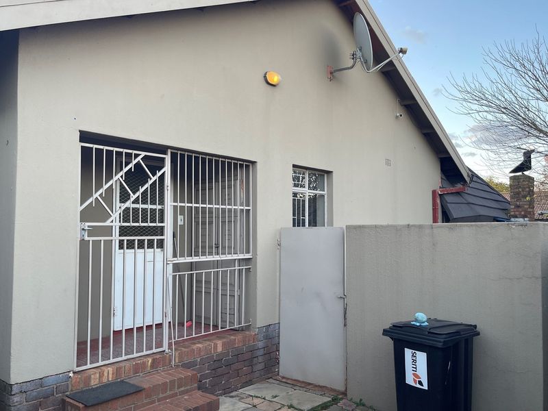 Exterior view of the property featuring a secure entrance with metal security gates, brick steps, and a side boundary wall.