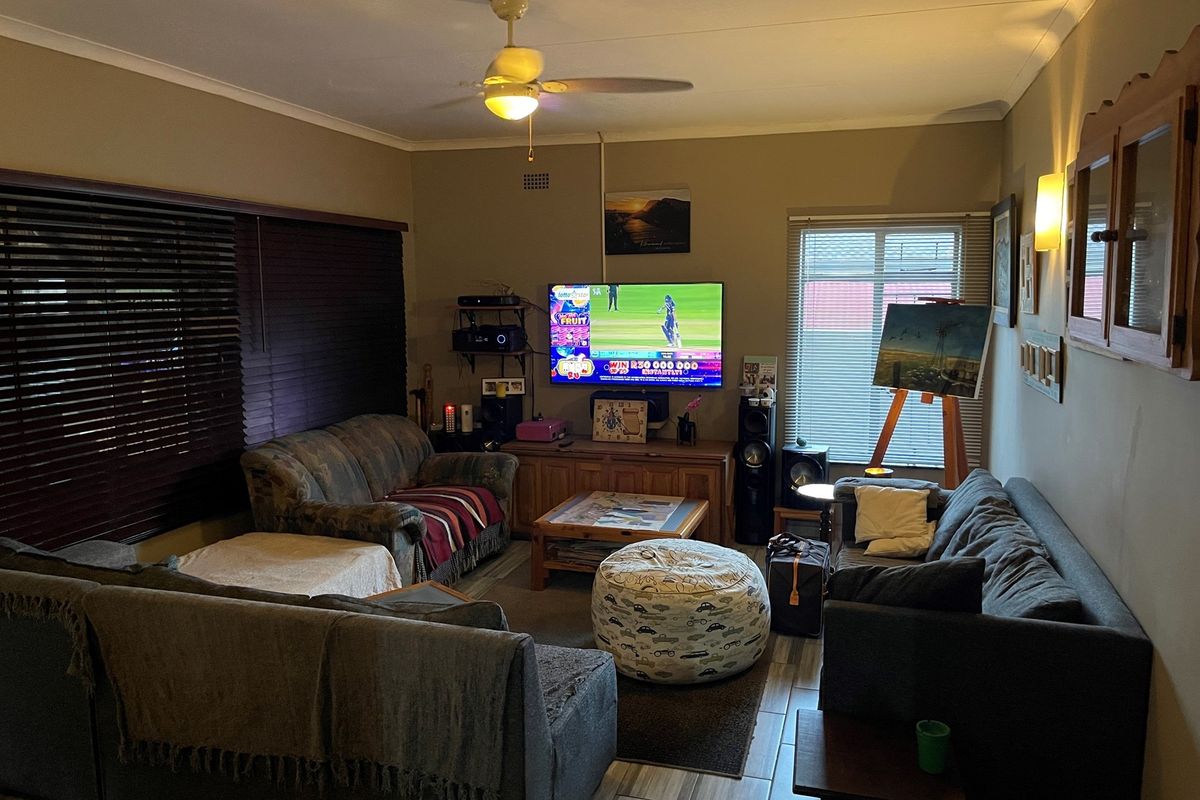 A comfortable living room featuring tiled flooring, a ceiling fan, and window blinds, providing a functional space for relaxation and entertainment.