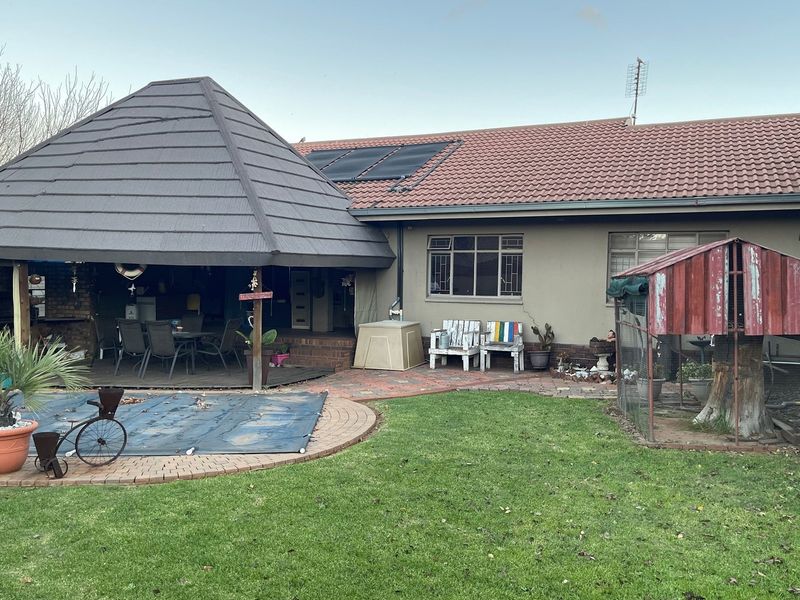 Rear view of the property featuring a covered patio area, swimming pool with cover, and a landscaped garden with a small enclosure.