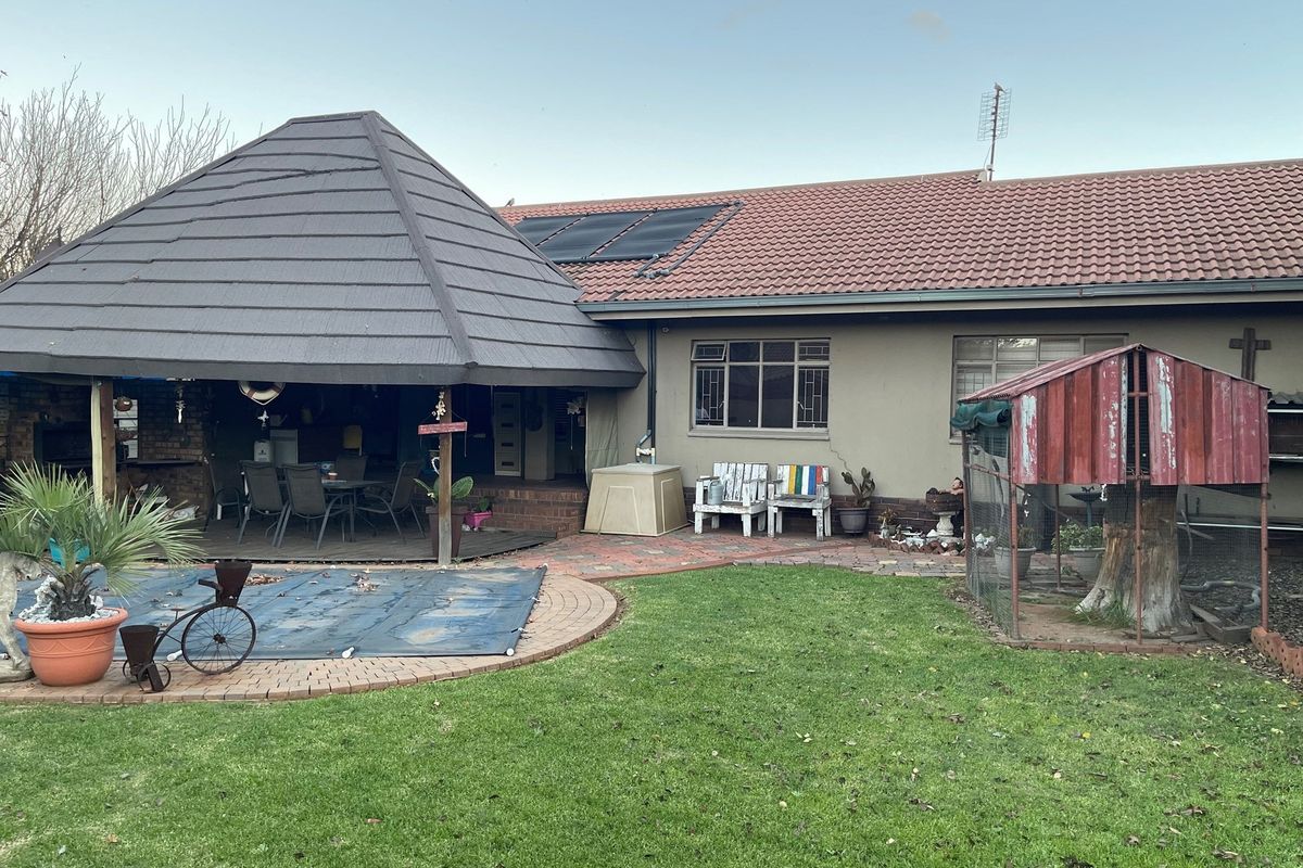 Rear view of the property featuring a covered patio area, swimming pool with cover, and a landscaped garden with a small enclosure.